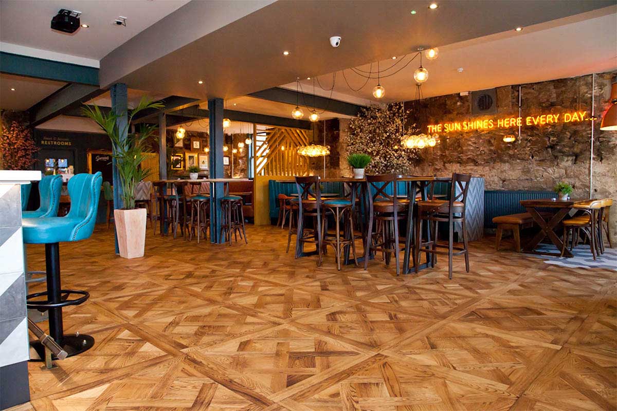 Basket weave parquet engineered wood floor inside an open-plan restaurant.